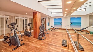 A gym with exercise equipment, a wooden floor, and a view of the beach through the windows. - Ilusion Markus & Spa (Santa Margalida)