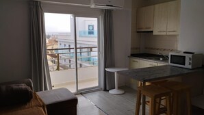 A modern kitchen with a microwave, wooden cabinets, and a view of a residential area through a sliding door. - Raxa (Palma de Mallorca)