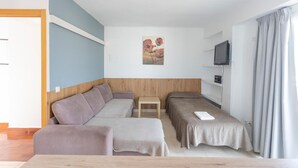 A modern room with a sofa, two single beds, a small table, a TV, and a painting on the wall. - Raxa (Palma de Mallorca)