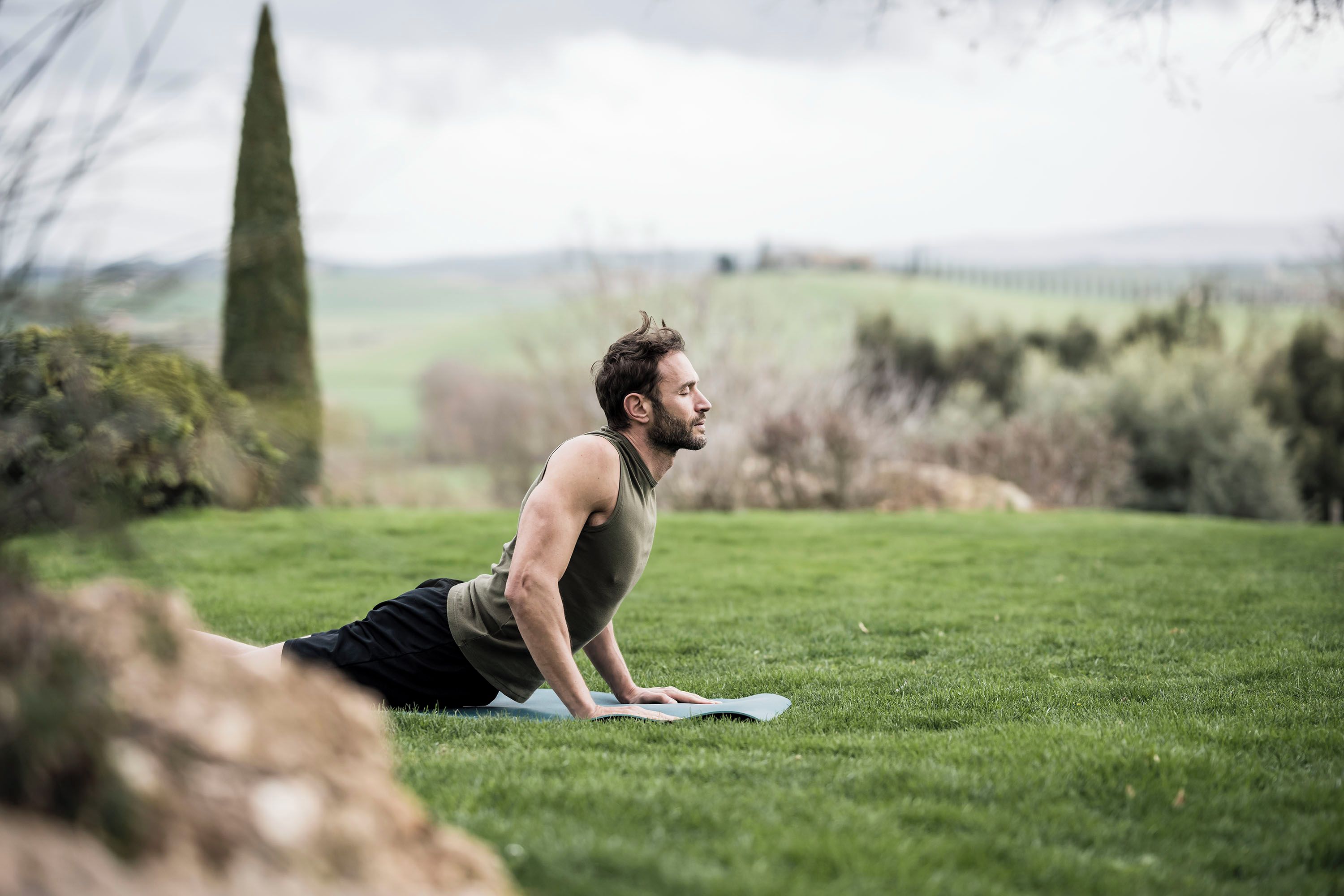 Une personne effectuant un exercice de planche sur un tapis de yoga, dans un environnement extérieur avec de l’herbe et des arbres.