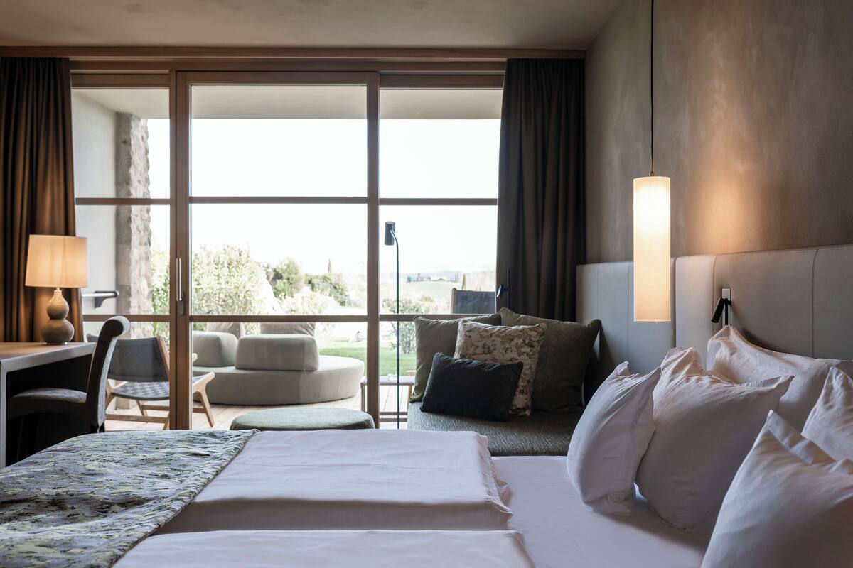 Une chambre d’hôtel équipée d’un lit, d’un bureau, d’une chaise, d’un canapé et d’une grande fenêtre donnant sur l’extérieur.