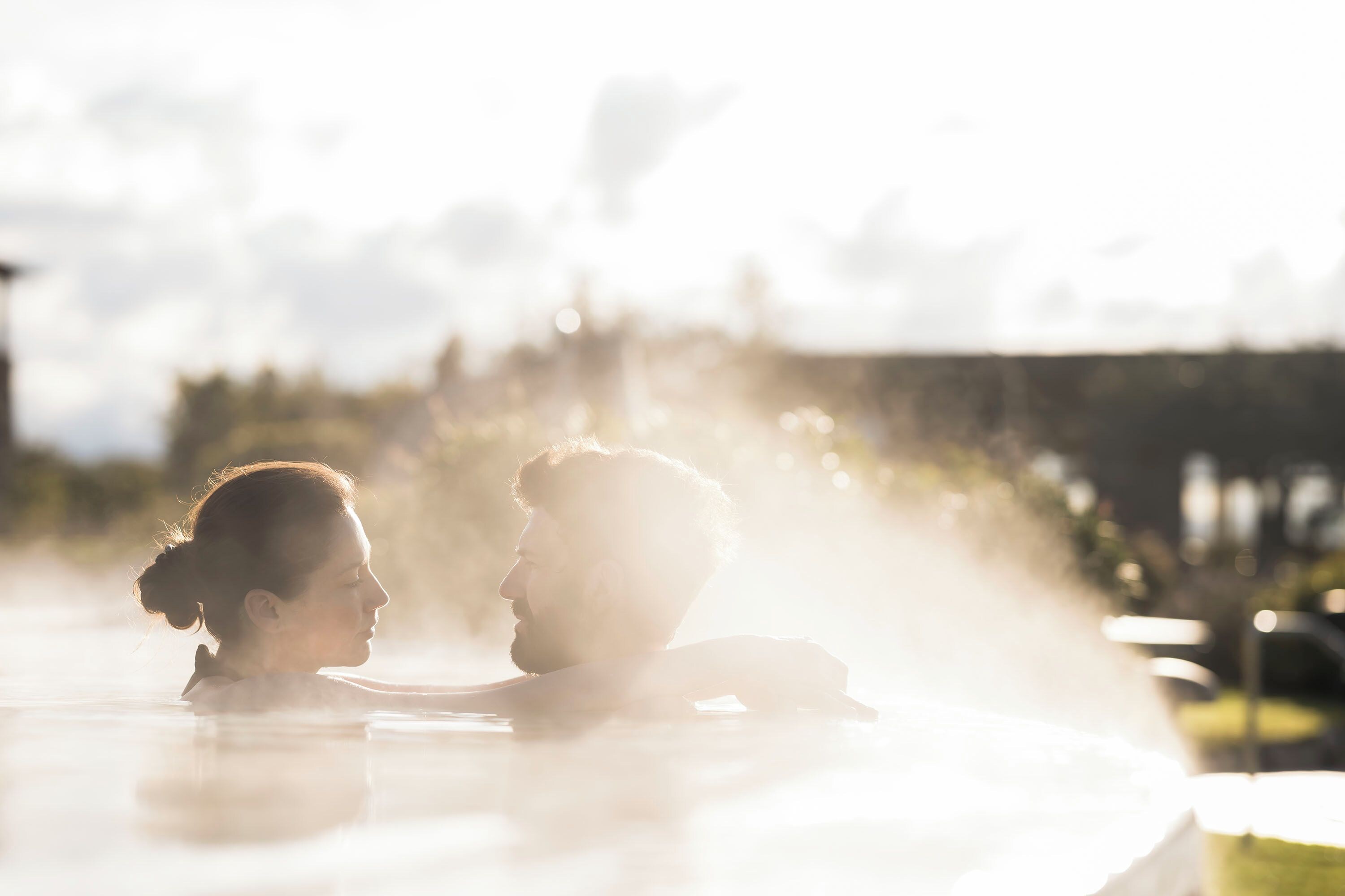 Ein Paar sitzt in einer Whirlpool-Badewanne, im Hintergrund verschwommene Außenbereiche.