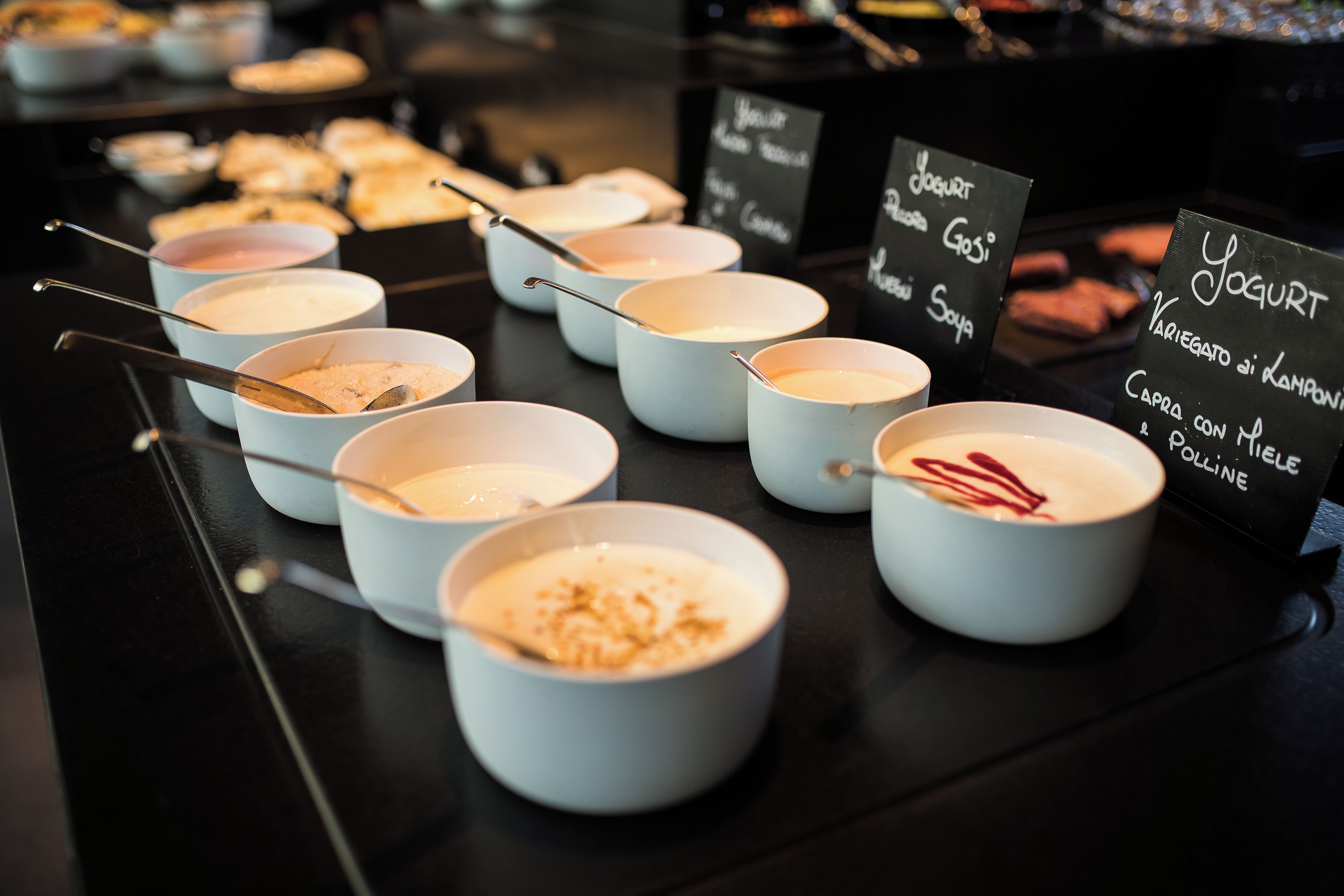 A selection of yogurt-based desserts in bowls with spoons, accompanied by a sign listing the flavors.
