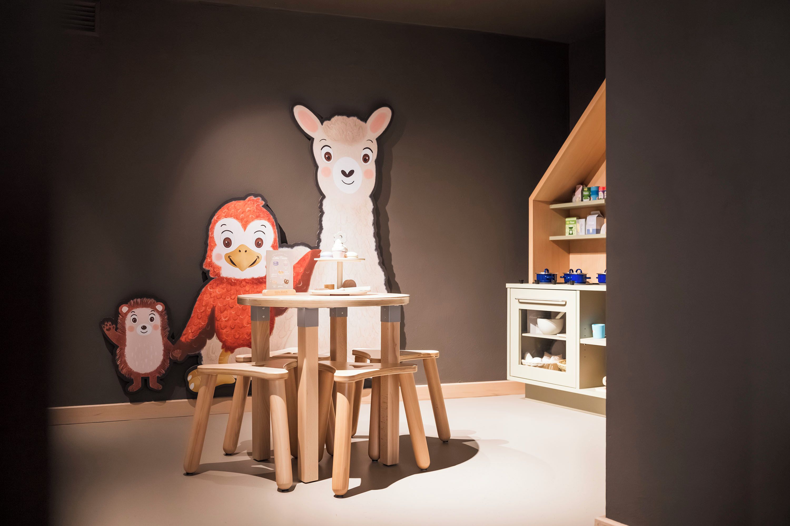 A children's play area with a table and chairs, a shelf with toys, and a wall with animal cutouts.