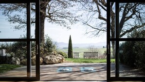 Habitación con ventanas amplias que dan a un jardín, con un tapete de yoga y un cojín blanco en el suelo.