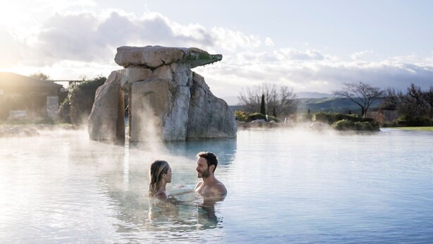 Una pareja en aguas termales, con una gran formación rocosa al fondo.