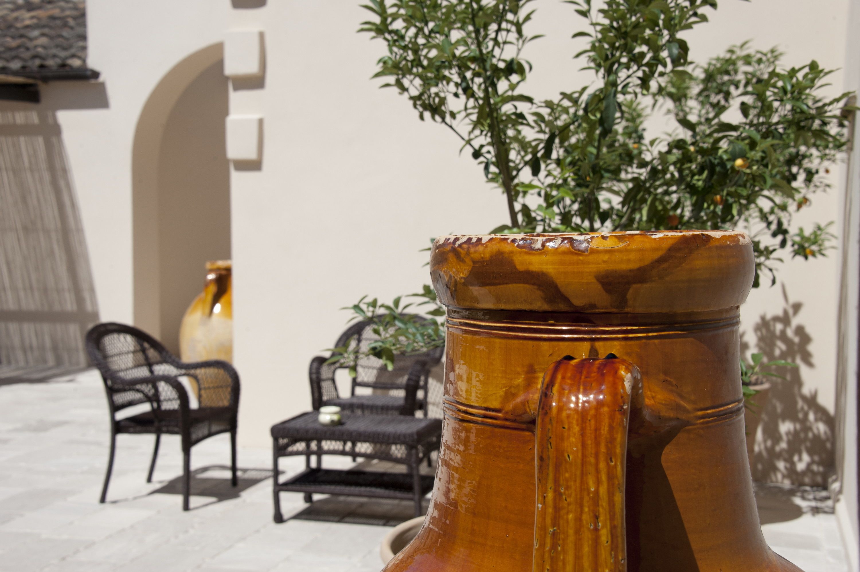 A large ceramic vase with a plant in a courtyard with outdoor furniture.
