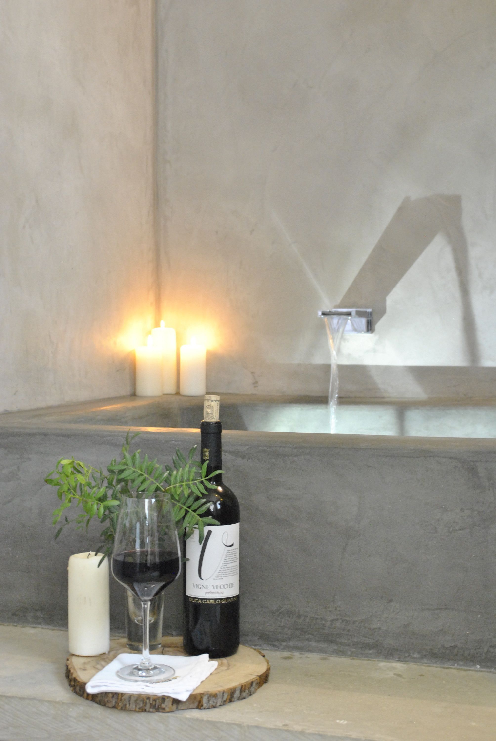 A bottle of wine, a glass, and a candle on a wooden coaster.