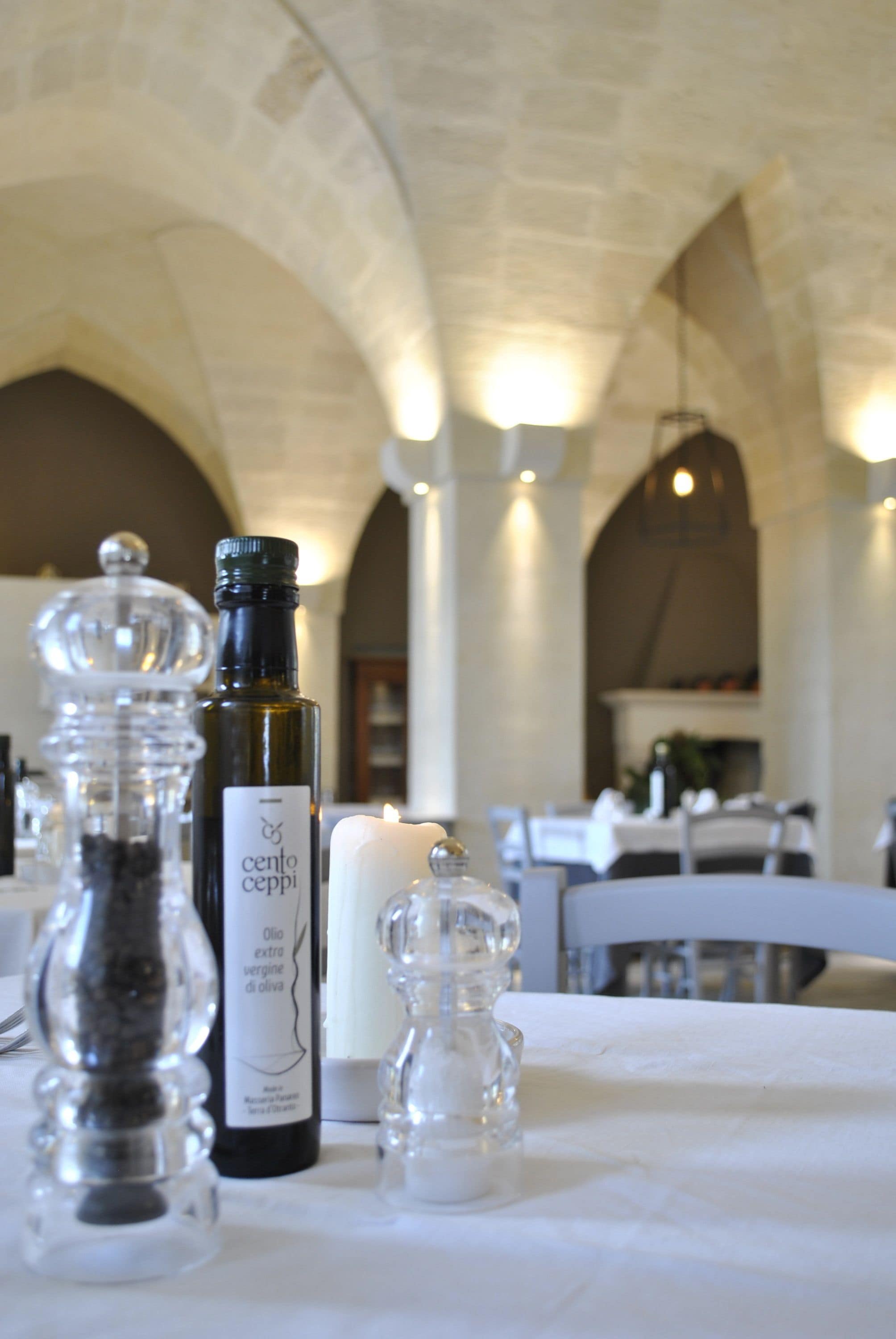 A table set with a bottle of Cento Ceppi extra virgin olive oil, salt and pepper shakers, and a candle.