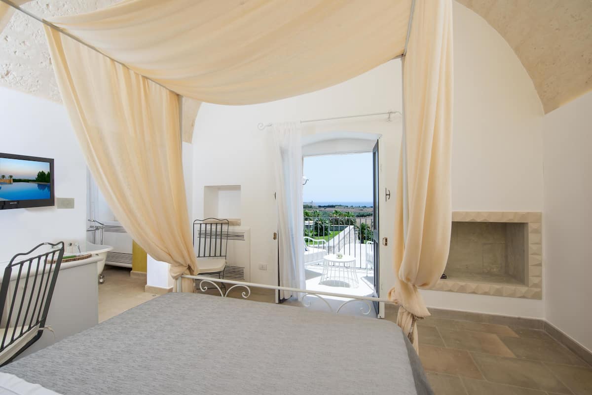 A bedroom with a bed, a television, a bathroom, and a balcony with a view.