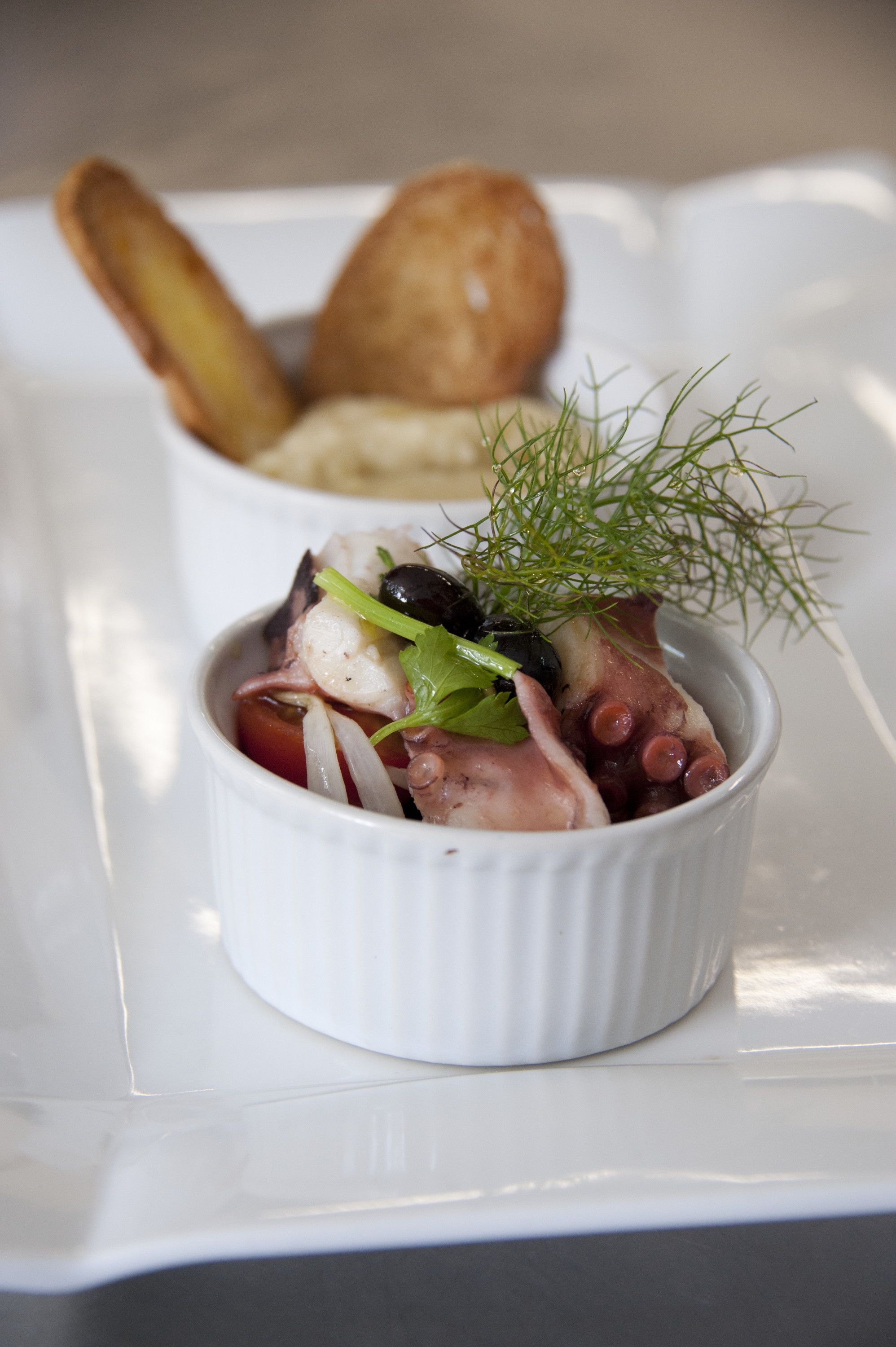 Eine weiße Keramikschale mit einem Seafood-Salat, garniert mit Dill, auf einem weißen Teller.