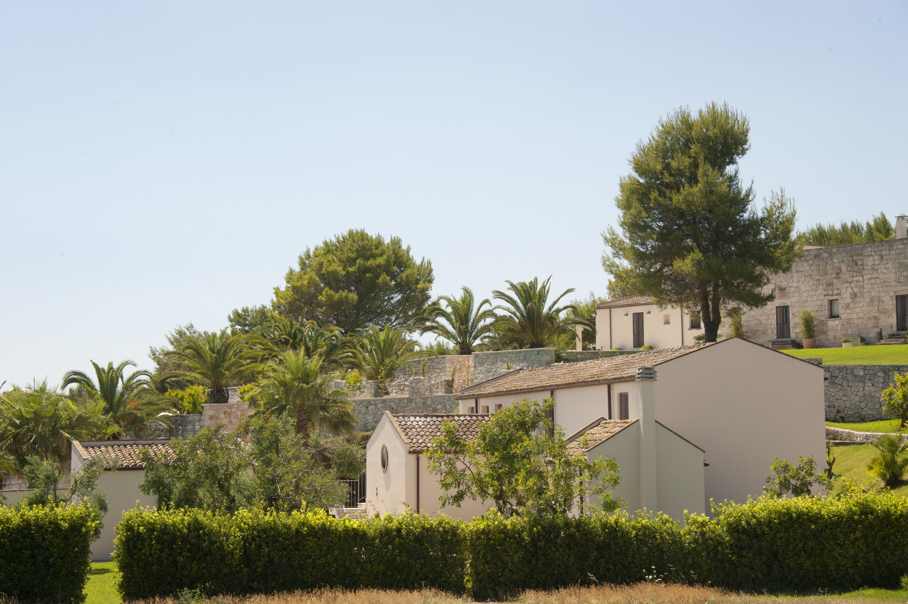 A traditional building with a stone wall, surrounded by well-maintained hedges and palm trees.