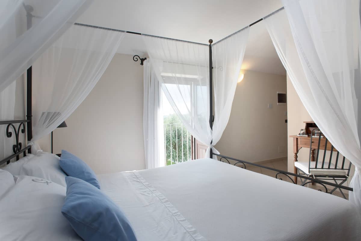 A bedroom with a four-poster bed, white linens, and sheer curtains.