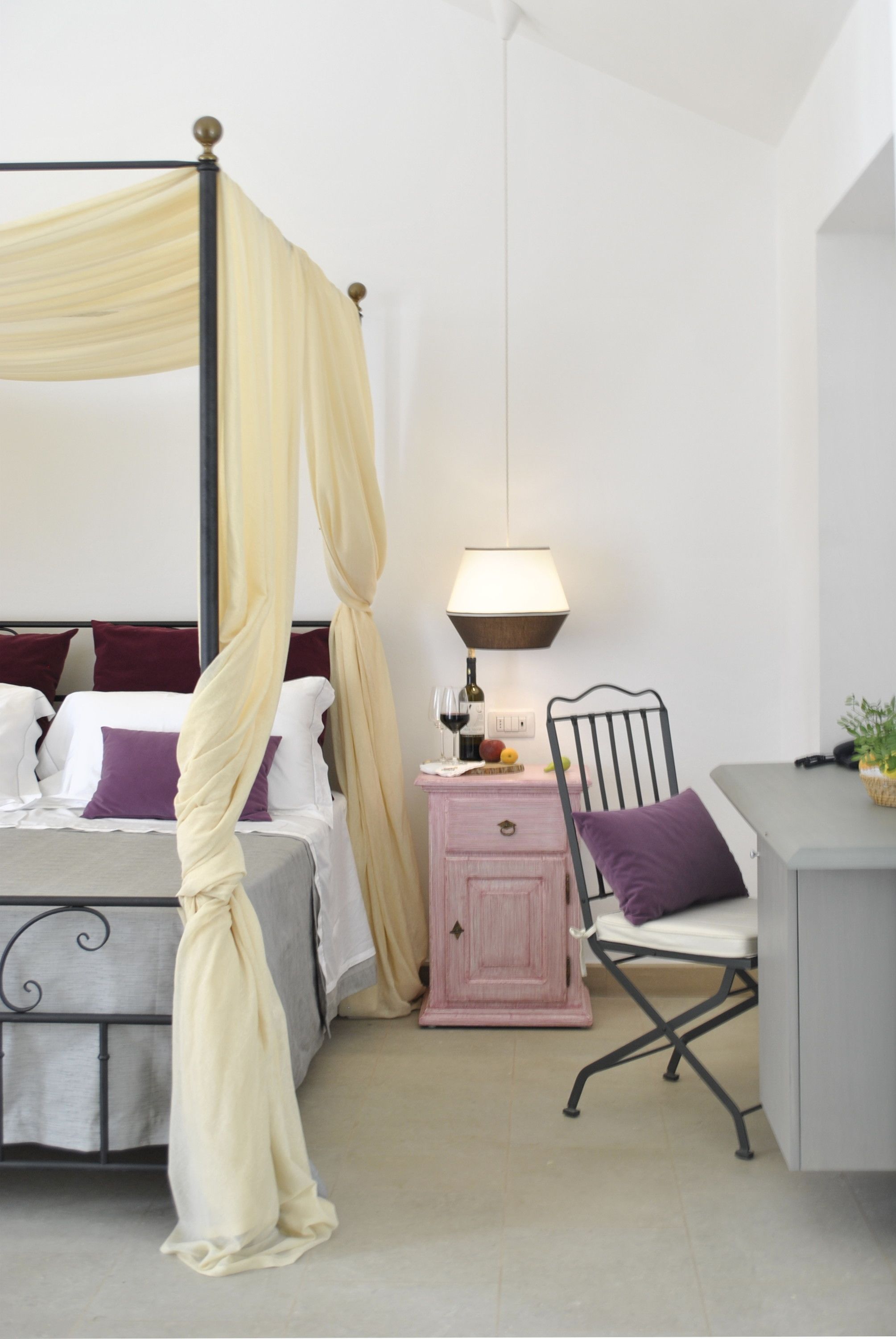 A four-poster bed with a canopy, a bedside table with a lamp, a chair, and a small cabinet.