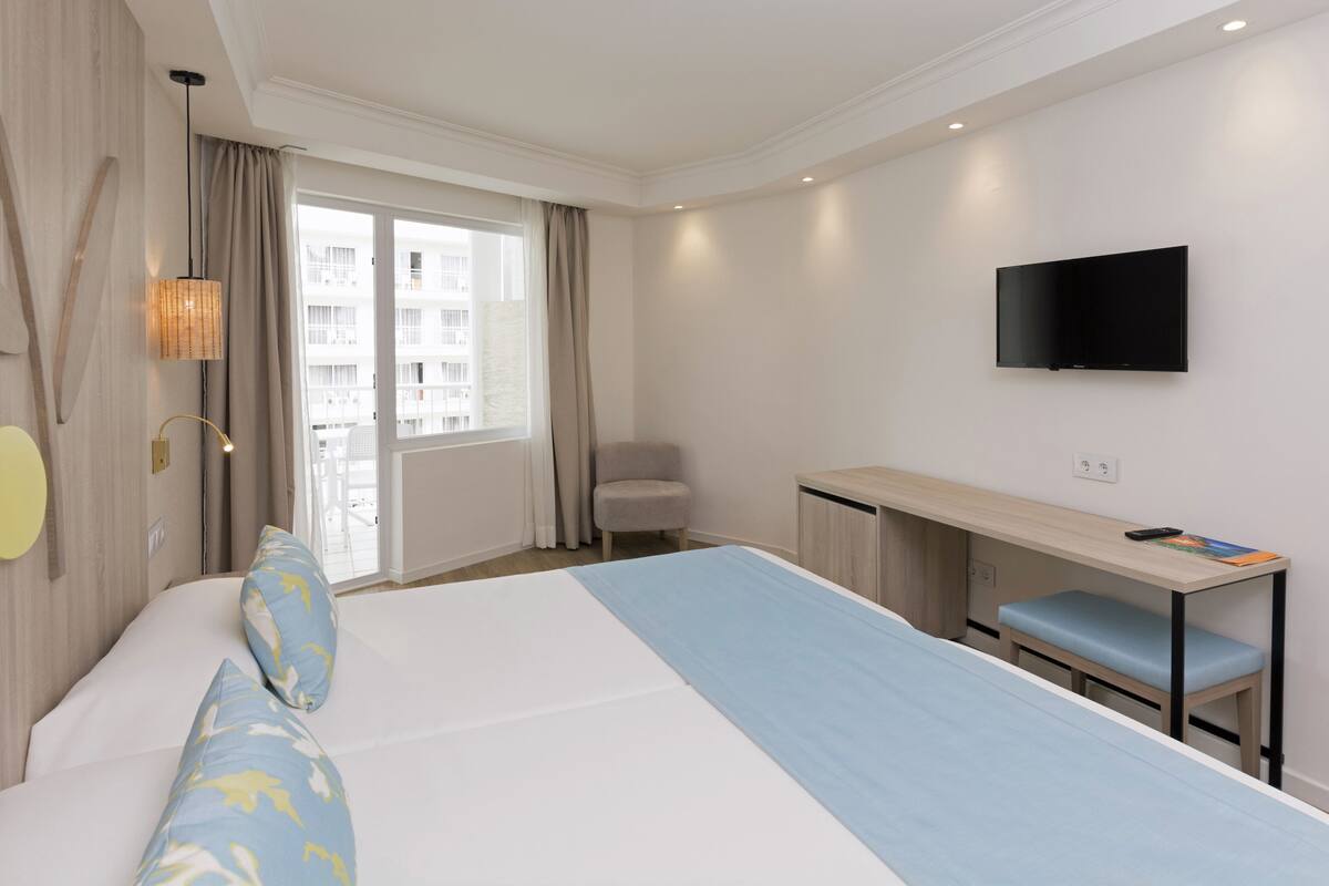 Hotellihuone, jossa on sänky, työpöytä, tuoli, televisio ja ikkuna, jossa on verhot.