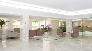 Vestíbulo con piso de mármol, una mesa de vidrio con un florero y áreas de estar con sillas.