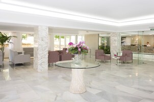 A lobby with a marble floor, a glass-top table with a vase of flowers, and seating areas with chairs.