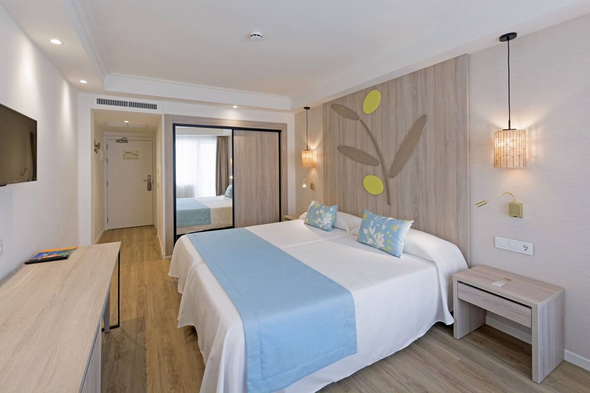 Moderni hotellihuone, jossa on suuri sänky, yöpöydät, työpöytä ja vaatekaappi.