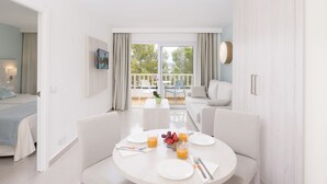 Una habitación de hotel moderna con comedor, un balcón y vistas, y una cama con colcha azul.