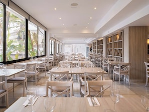 A spacious restaurant with multiple tables and chairs, large windows with a view of greenery, and a modern interior design.