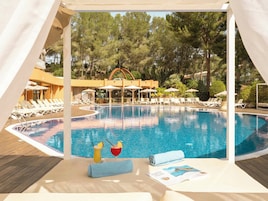 Un área de piscina con sillones de descanso y sombrillas, rodeada de árboles.