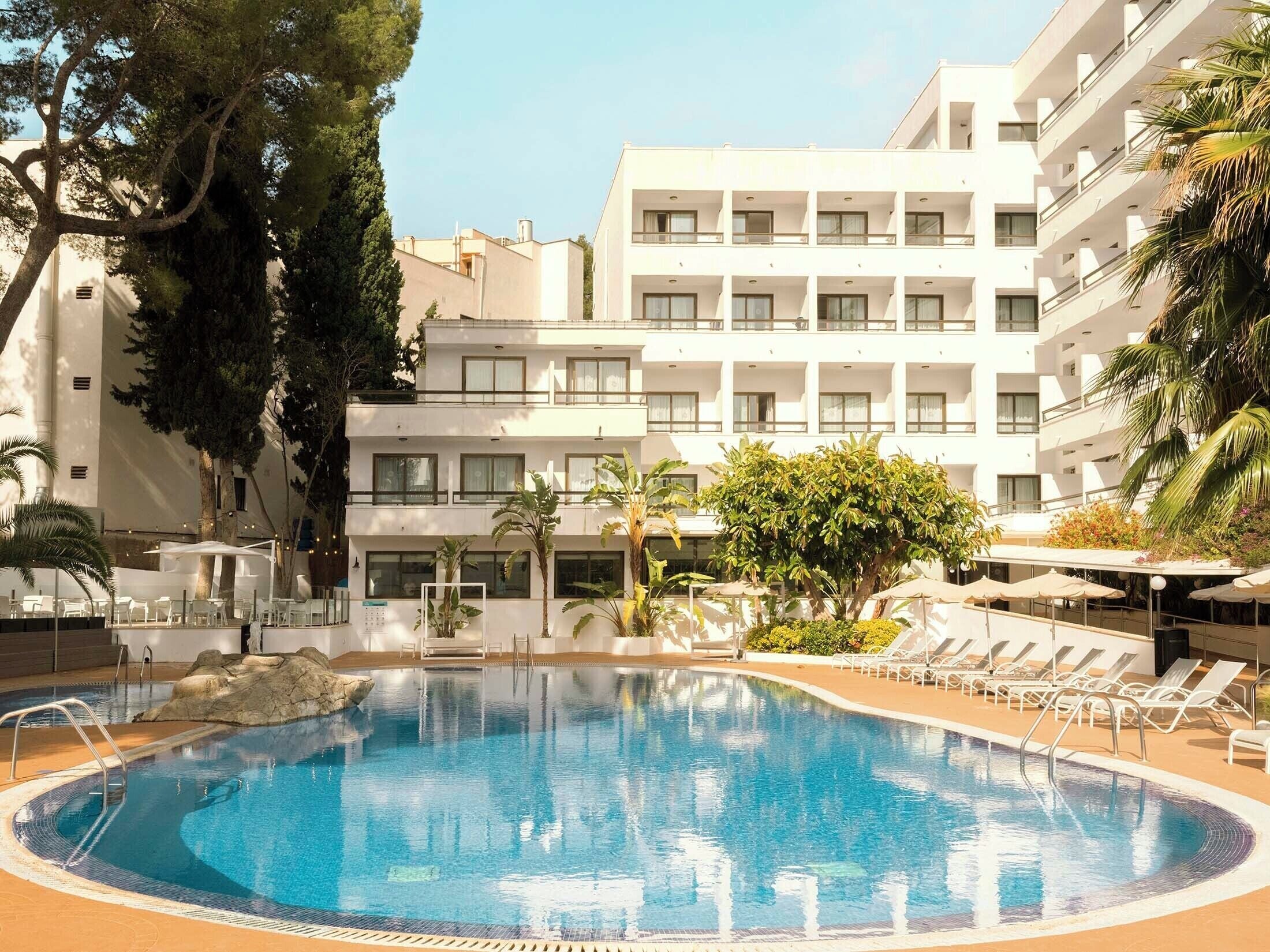 A hotel with a swimming pool surrounded by lounge chairs and palm trees.