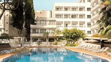 A hotel with a swimming pool surrounded by lounge chairs and palm trees.
