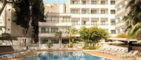 A hotel with a swimming pool surrounded by lounge chairs and palm trees.