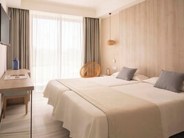 Habitación de hotel con dos camas, un escritorio, una silla y un ventanal con cortinas.