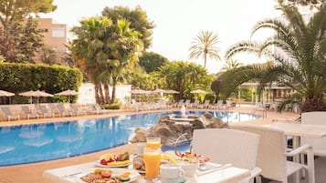 A poolside breakfast setup with a table, chairs, and a variety of food and drinks.