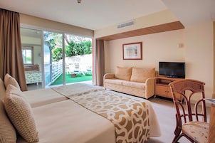 Habitación de hotel con cama, sofá, televisión y zona de comedor con mesa y sillas.