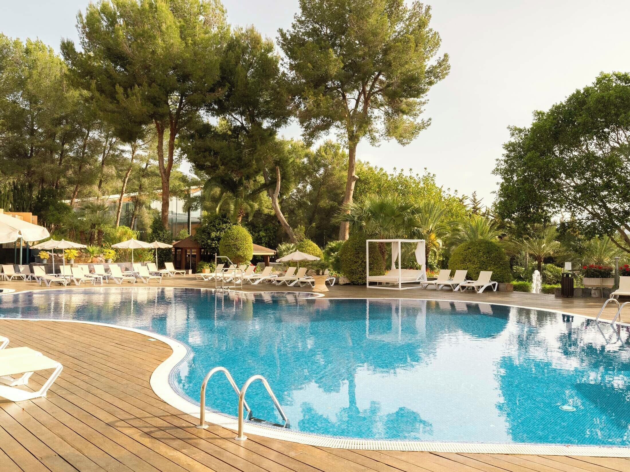 A swimming pool with lounge chairs and umbrellas, surrounded by trees.