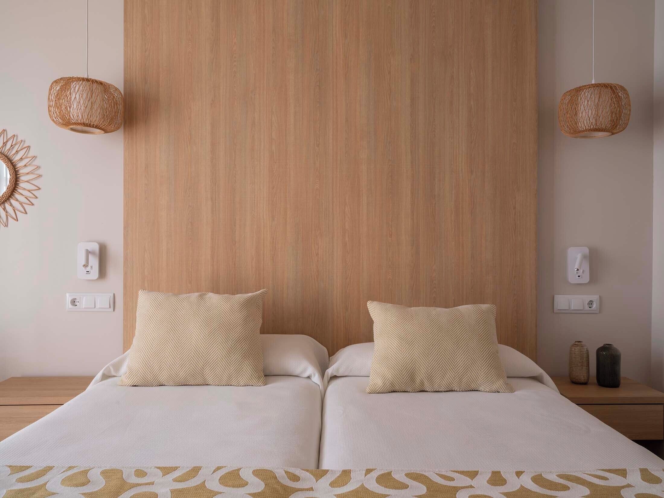 A double bed with two pillows, a wooden headboard, bedside lamps, and a decorative wall piece.