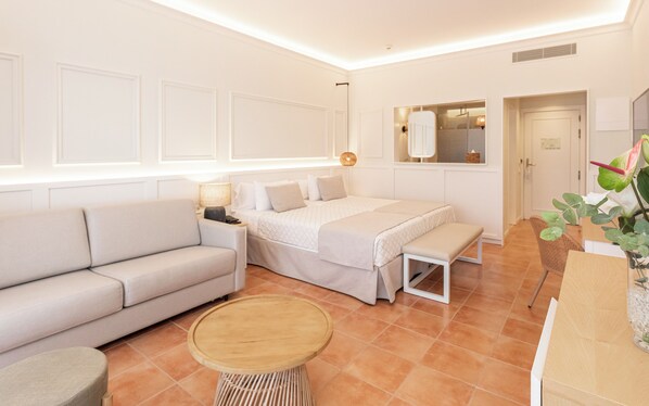 Una habitación de hotel moderna con sofá, cama, una mesa redonda de madera y un espejo.