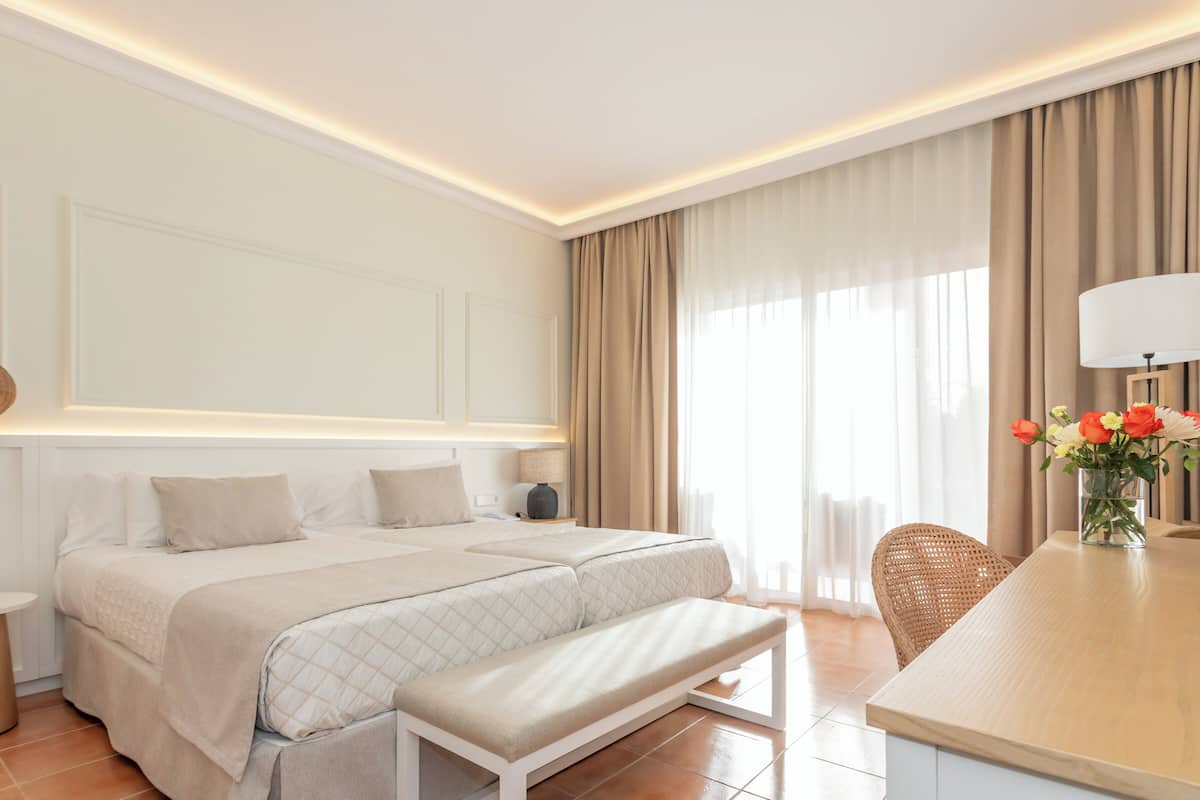 Une chambre d’hôtel moderne avec un grand lit, des tables de chevet, un banc, un bureau et un vase de fleurs.