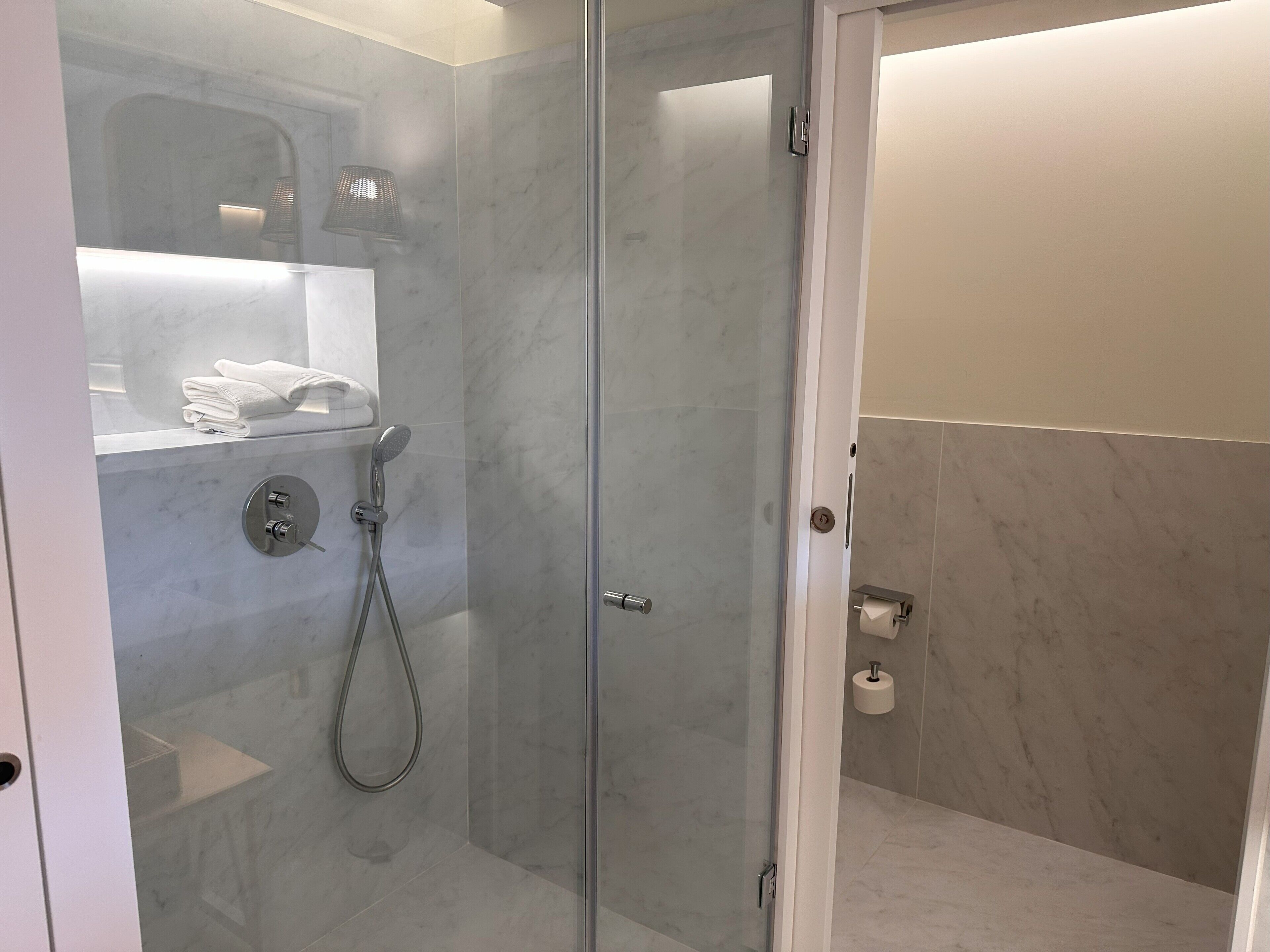 Une salle de bain moderne avec une douche à parois de verre, des murs en marbre et un porte-rouleau de papier toilette.