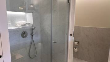 Een moderne badkamer met een douche met glazen wanden, marmeren wanden en een toiletrolhouder.