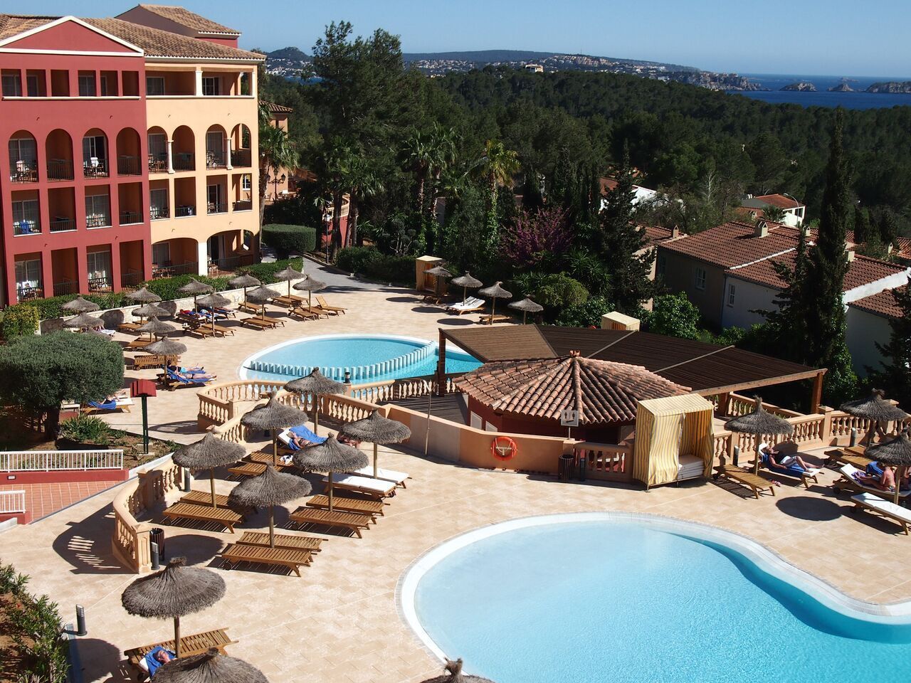 A resort with multiple swimming pools, sun loungers, and a large building with balconies.