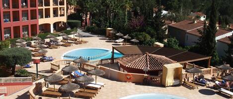 A resort with multiple swimming pools, sun loungers, and a large building with balconies.