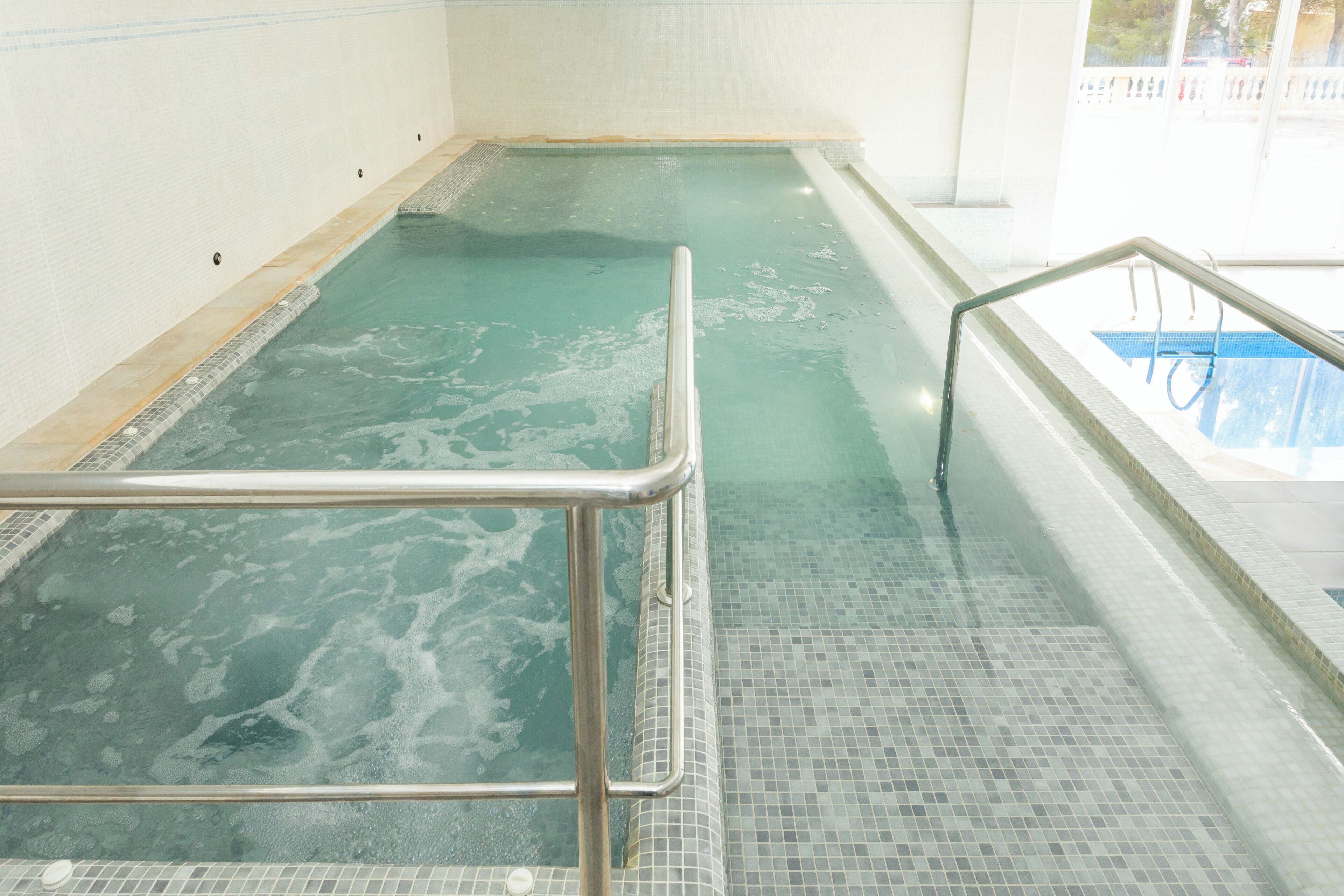A swimming pool with a tiled floor and a metal handrail.