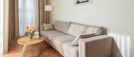 A modern living room with a beige sofa, a round wooden coffee table with a vase of flowers, and a lamp.