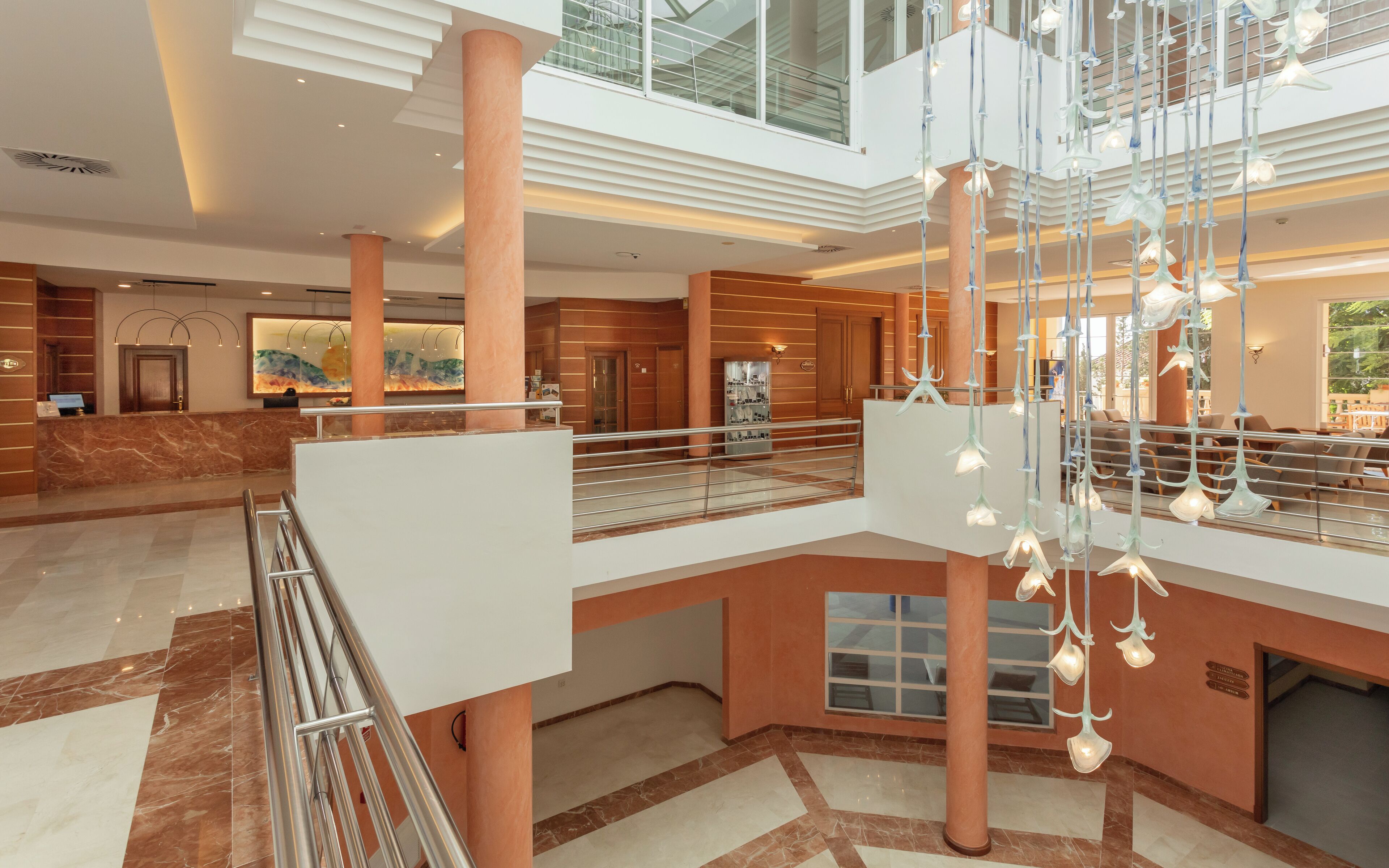 A spacious lobby with marble flooring, a reception desk, and a glass railing overlooking the lower level.