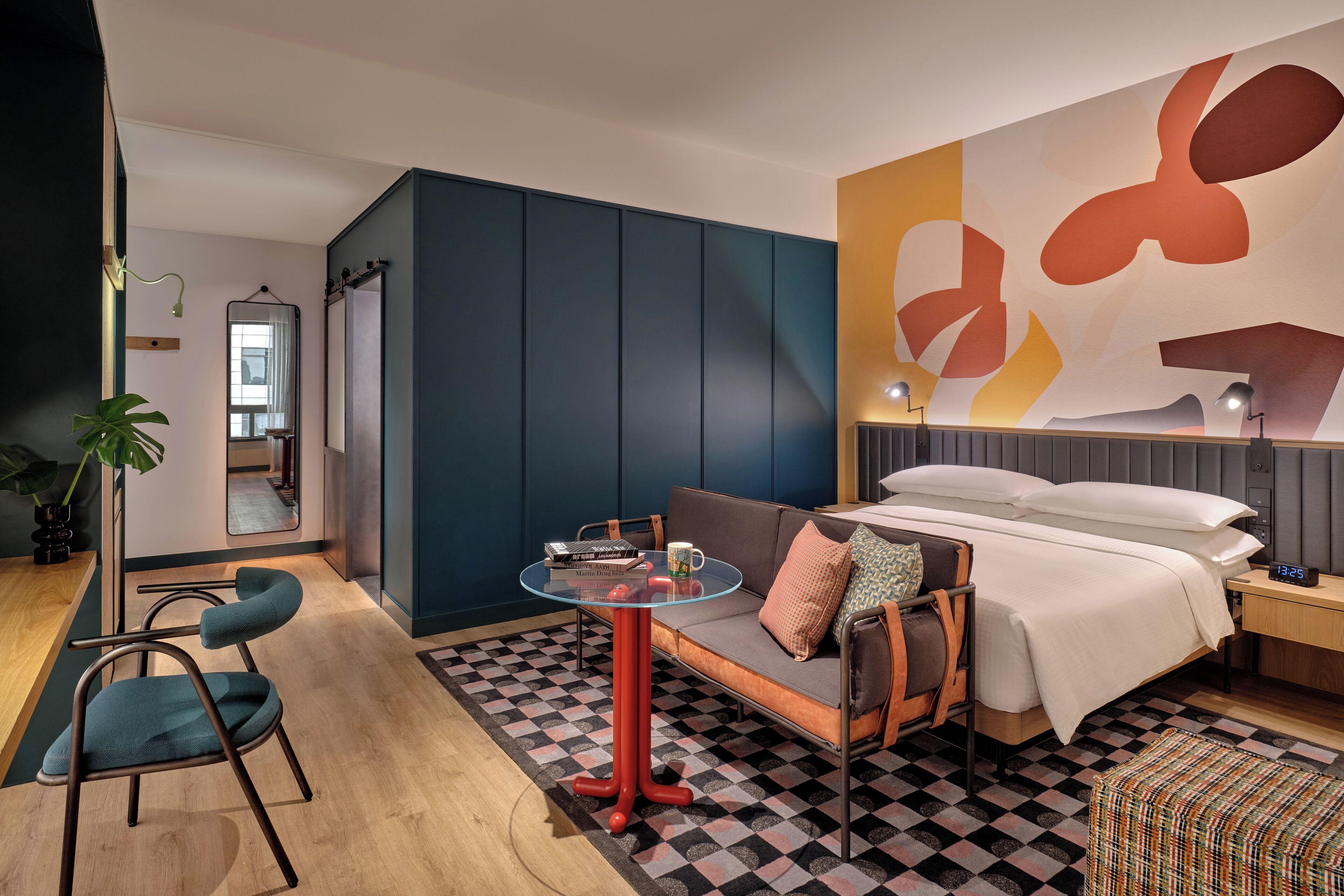 A modern hotel room with a checkered floor, a sofa, a glass table, and a bed with a large abstract wall art piece.