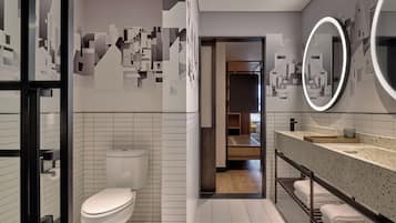 Un baño moderno con inodoro, lavamanos con espejo y zona de ducha.