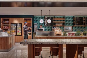 Interior moderno de una cafetería con barra, asientos, una vitrina refrigerada y una pizarra de menú.
