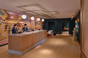 A reception desk with two staff members, a check-in counter, a wall with a colorful mural, and a modern ceiling design.