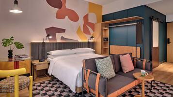A modern hotel room with a bed, sofa, and a small table with a cup.