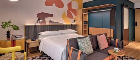 A modern hotel room with a bed, sofa, and a small table with a cup.