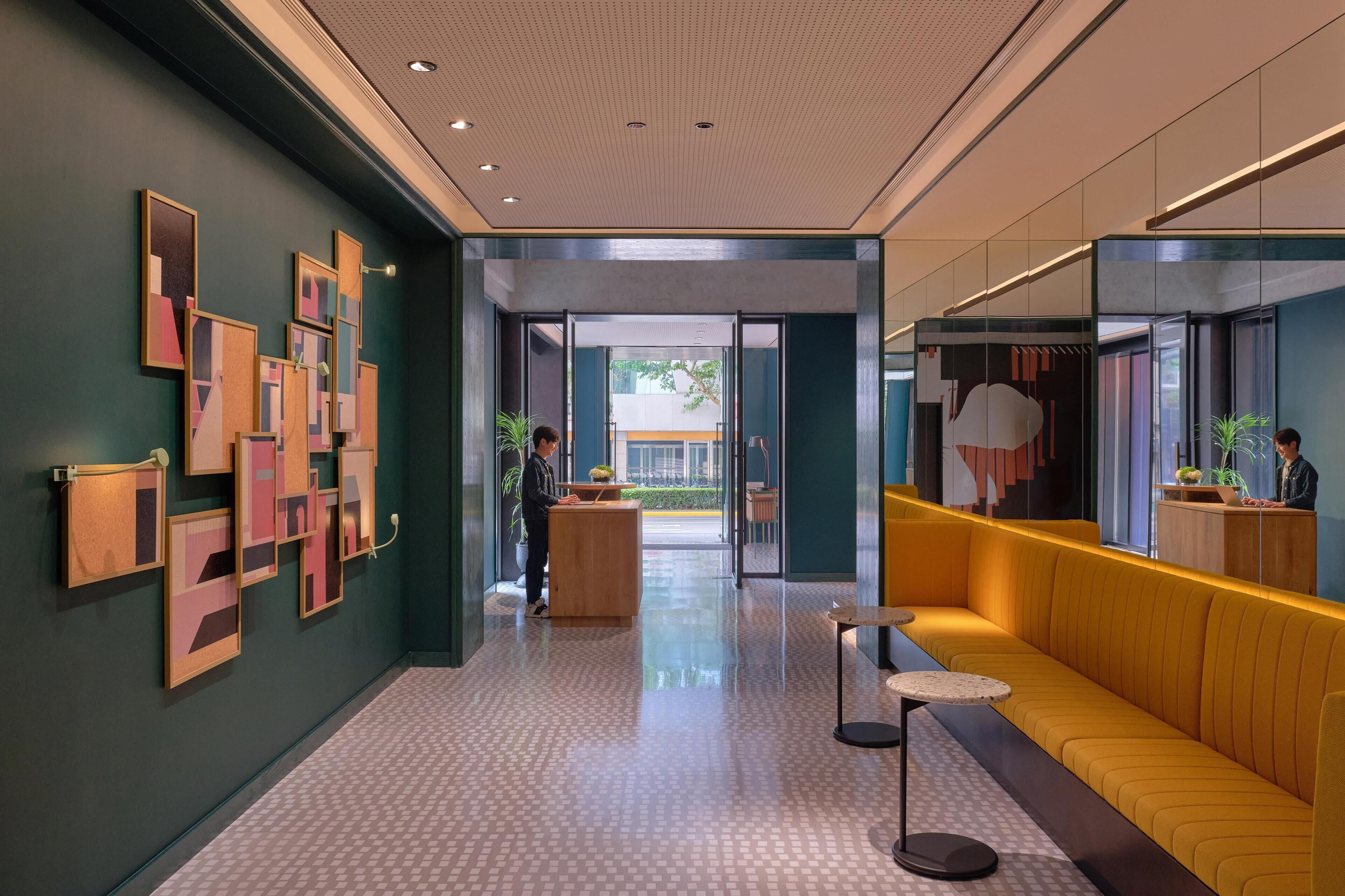 Een moderne lobby met een receptiebalie, een geel zitgedeelte en kunstwerken aan de muren.