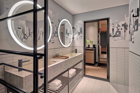 A modern bathroom with a large mirror, two circular lights, a countertop with a sink, and a towel rack.